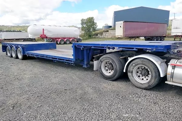 Lowboy trailer designed for hauling heavy construction machinery.