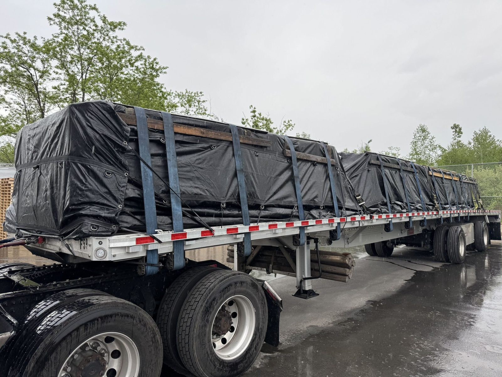 Flatbed load covered with black tarps on a wet road after rain