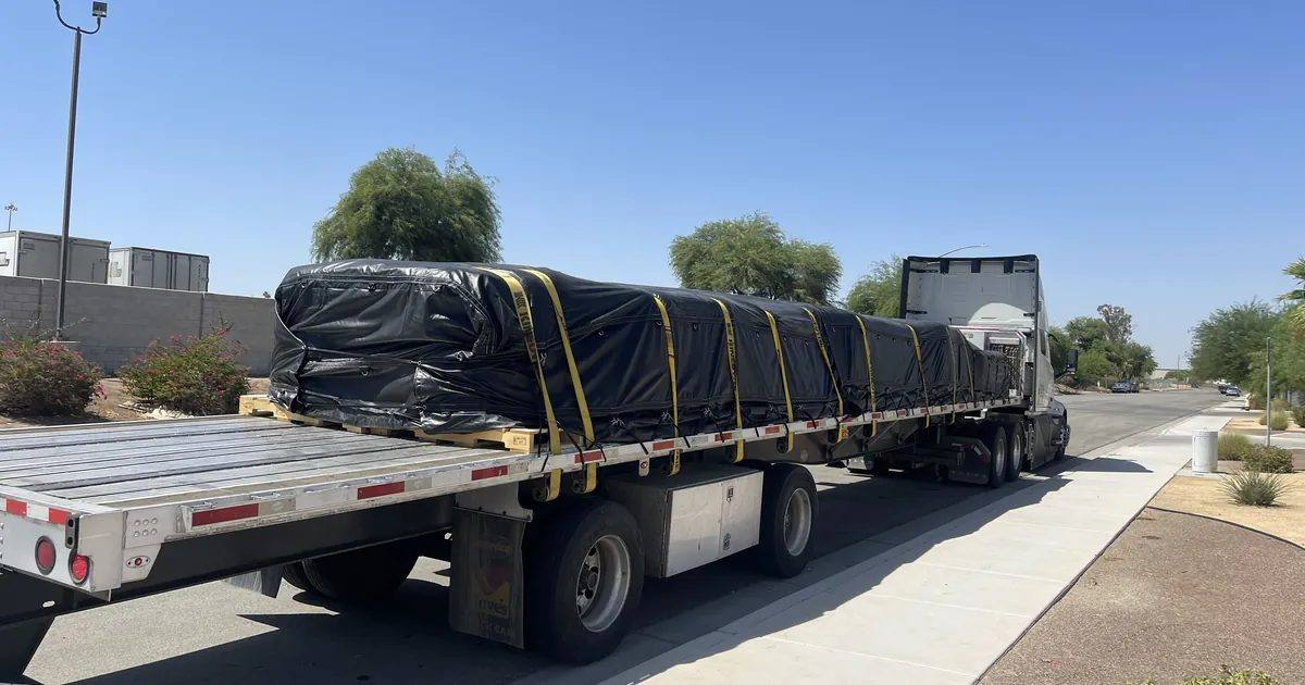 Semi truck with a tarped, strapped flatbed load parked along a street