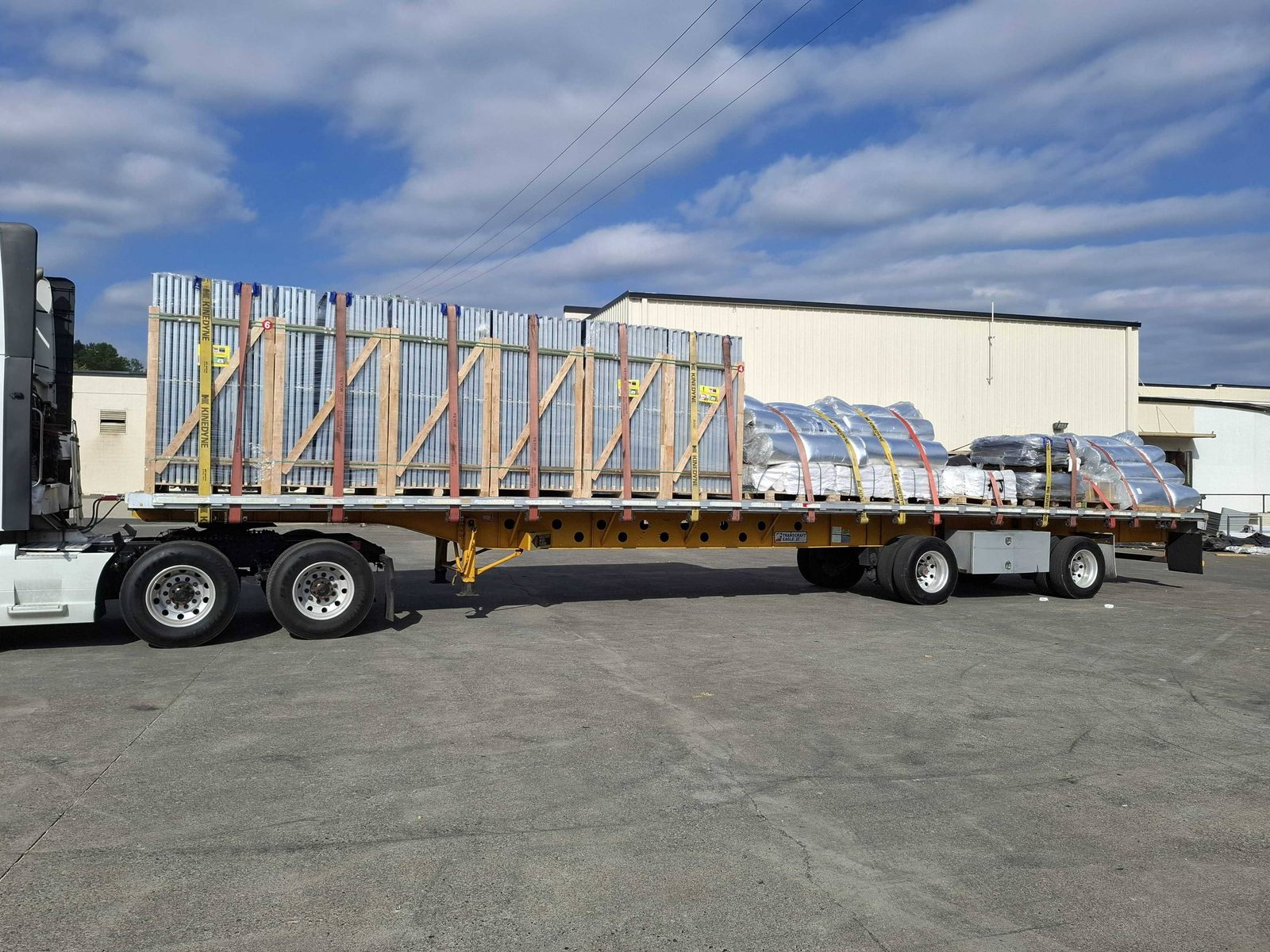 Flatbed trailer with crated panels and shrink-wrapped pallets of mixed freight in a yard