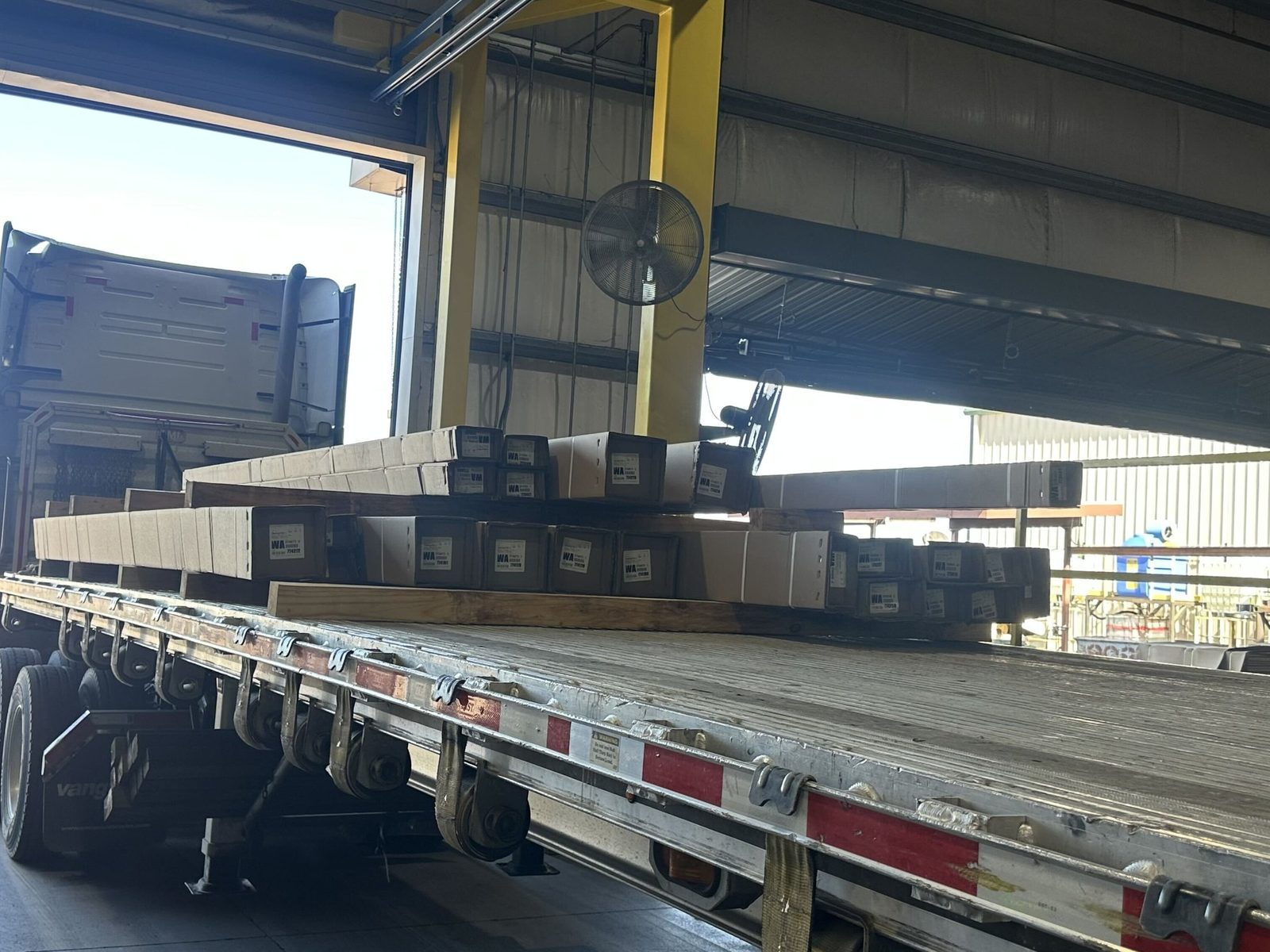 Flatbed trailer being loaded with crated building materials at a warehouse dock door
