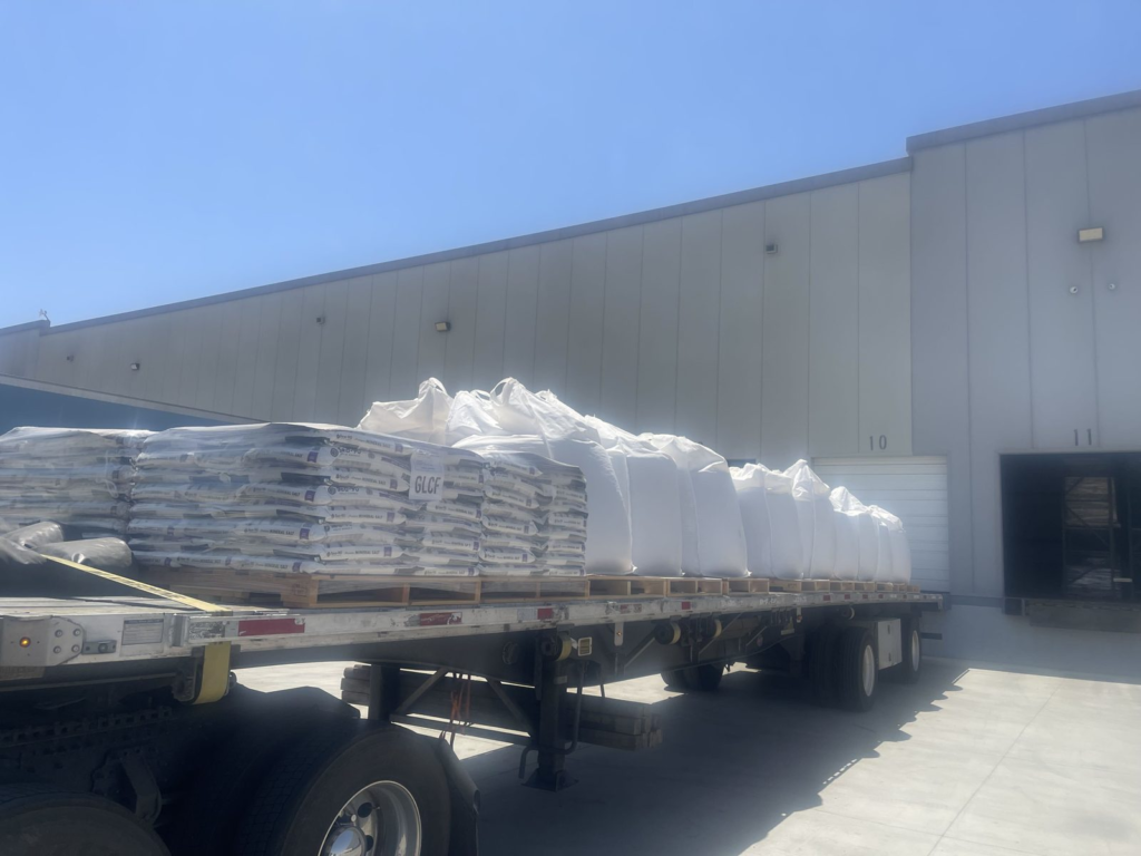 Flatbed trailer loaded with palletized bags beside a warehouse