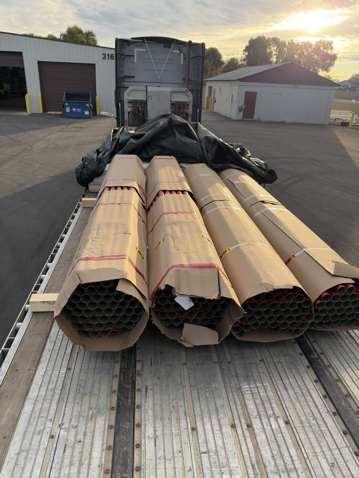 Cardboard-wrapped pipe bundles strapped on a flatbed trailer deck at sunset