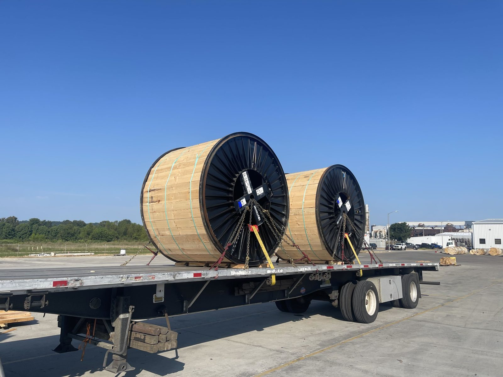 Two large wooden cable reels chained and strapped on a flatbed trailer