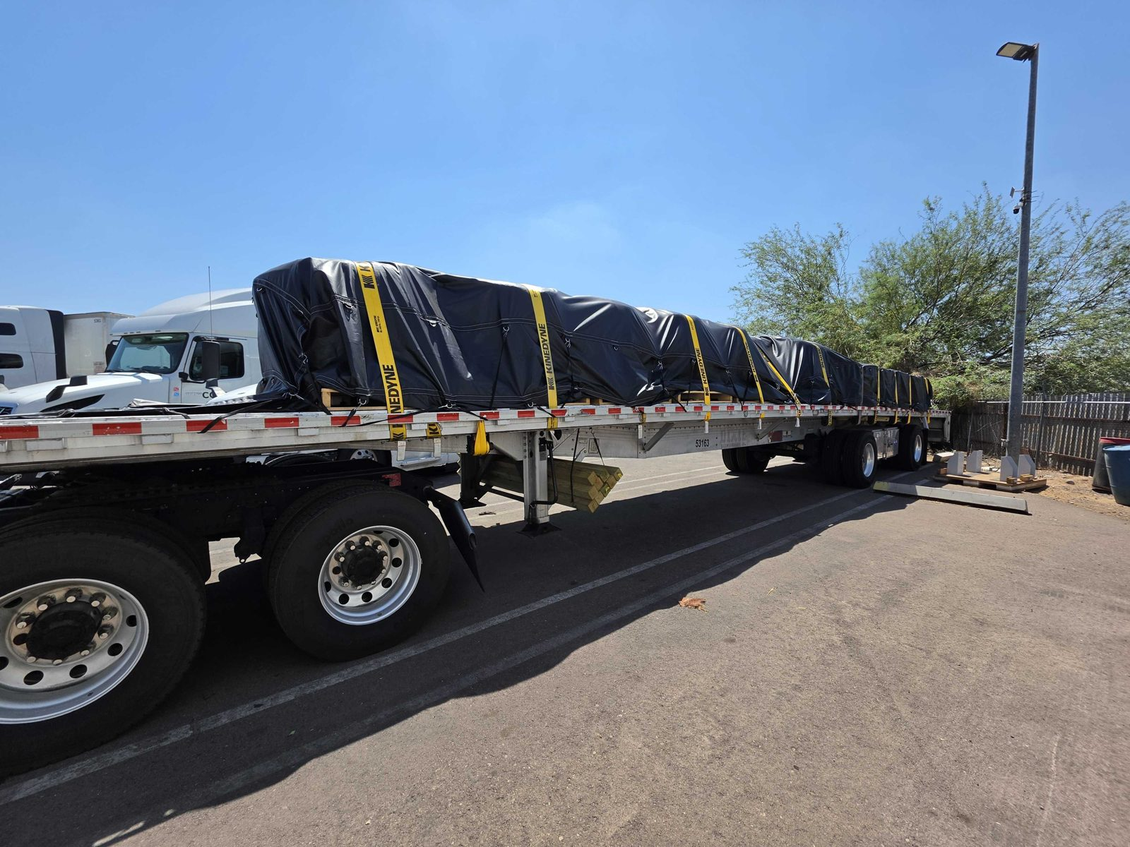Rear-quarter view of a flatbed trailer with a black tarped load and yellow straps
