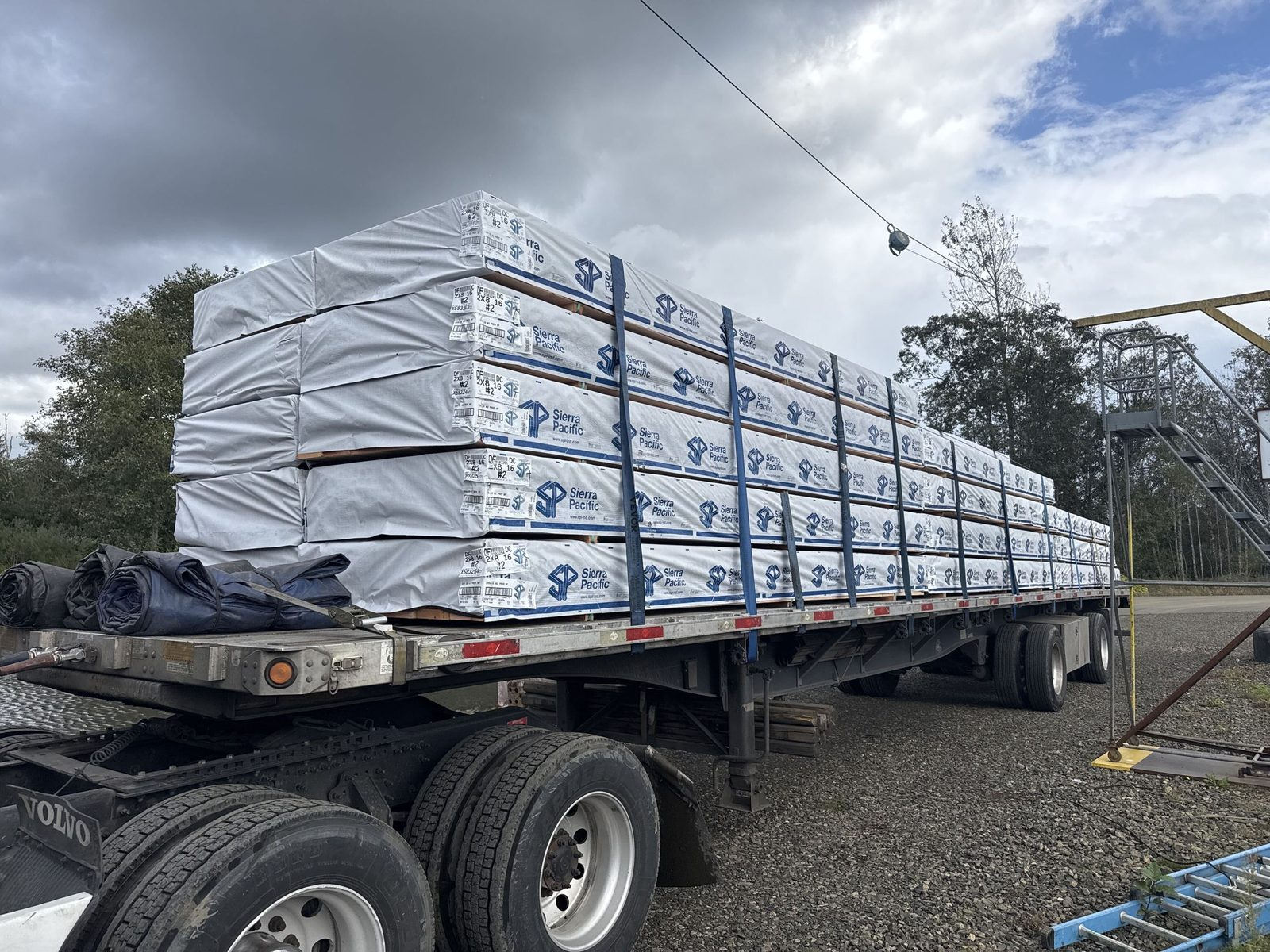 Flatbed trailer loaded with shrink-wrapped lumber bundles under a cloudy sky