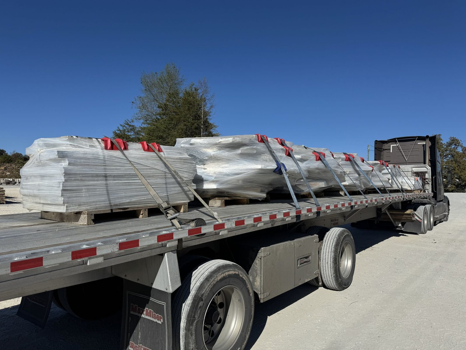 Flatbed trailer with shrink-wrapped pallets secured by straps and red edge protectors